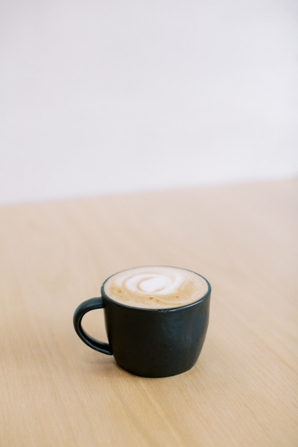 Image of a coffee cup with decorative foam sitting on a light colored wood table.