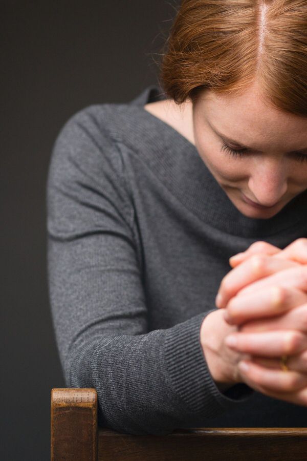 Young woman with red hair kneeling at a pew, praying.